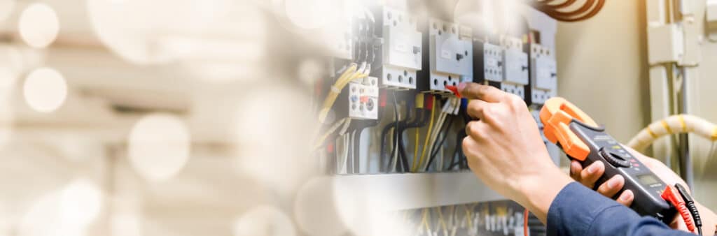 Un électricien utilise une pince ampèremétrique pour tester les composants d'un tableau électrique industriel.