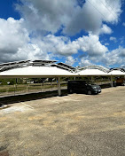 Ombrières de parking photovoltaïques blanches sous un ciel nuageux avec une voiture noire stationnée.