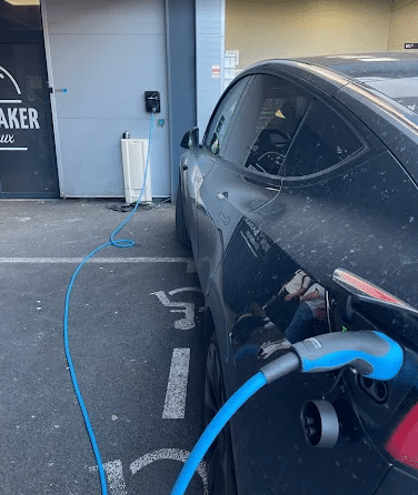 Recharge voiture électrique sur place handicapé devant Baker Tesla noire en charge avec câble bleu sur une place handicapé devant le commerce Baker.